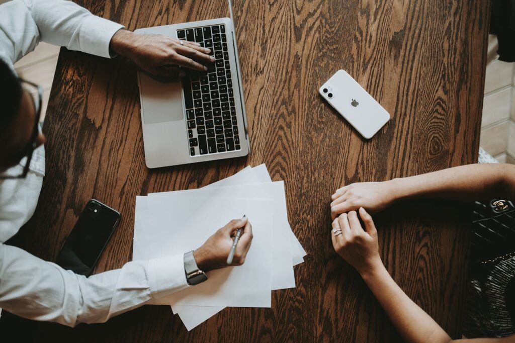 Two professionals collaborating in an office setting, using laptop and documents on a wooden table.